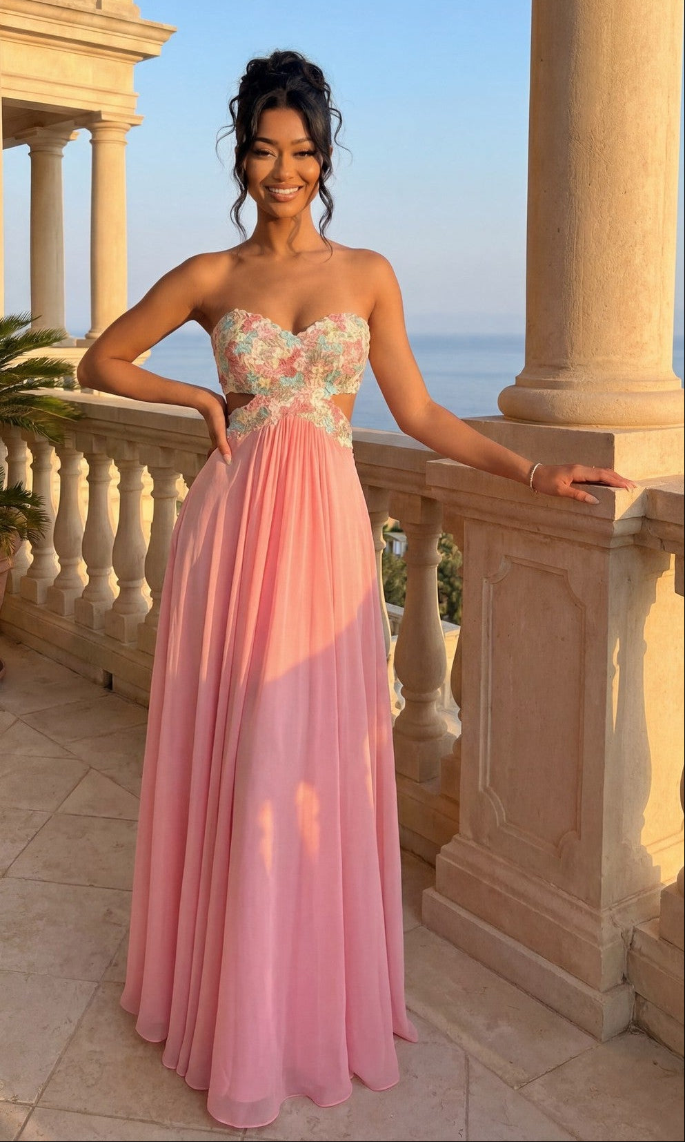A woman smiles at the camera on a stone balcony with a seaside view, wearing the La Femme Multicolor-Lace Chiffon Prom Dress 20059 in Sherbert, featuring a strapless chiffon skirt and floral lace-embroidered bodice.