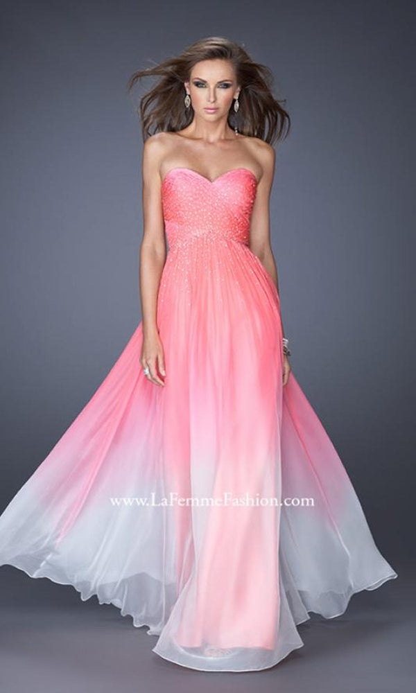 A woman stands against a plain gray background wearing the Floor Length La Femme Formal Dressâ€”a strapless, sweetheart neckline gown with a pink-to-white ombre, fitted beaded bodice and flowing skirt.