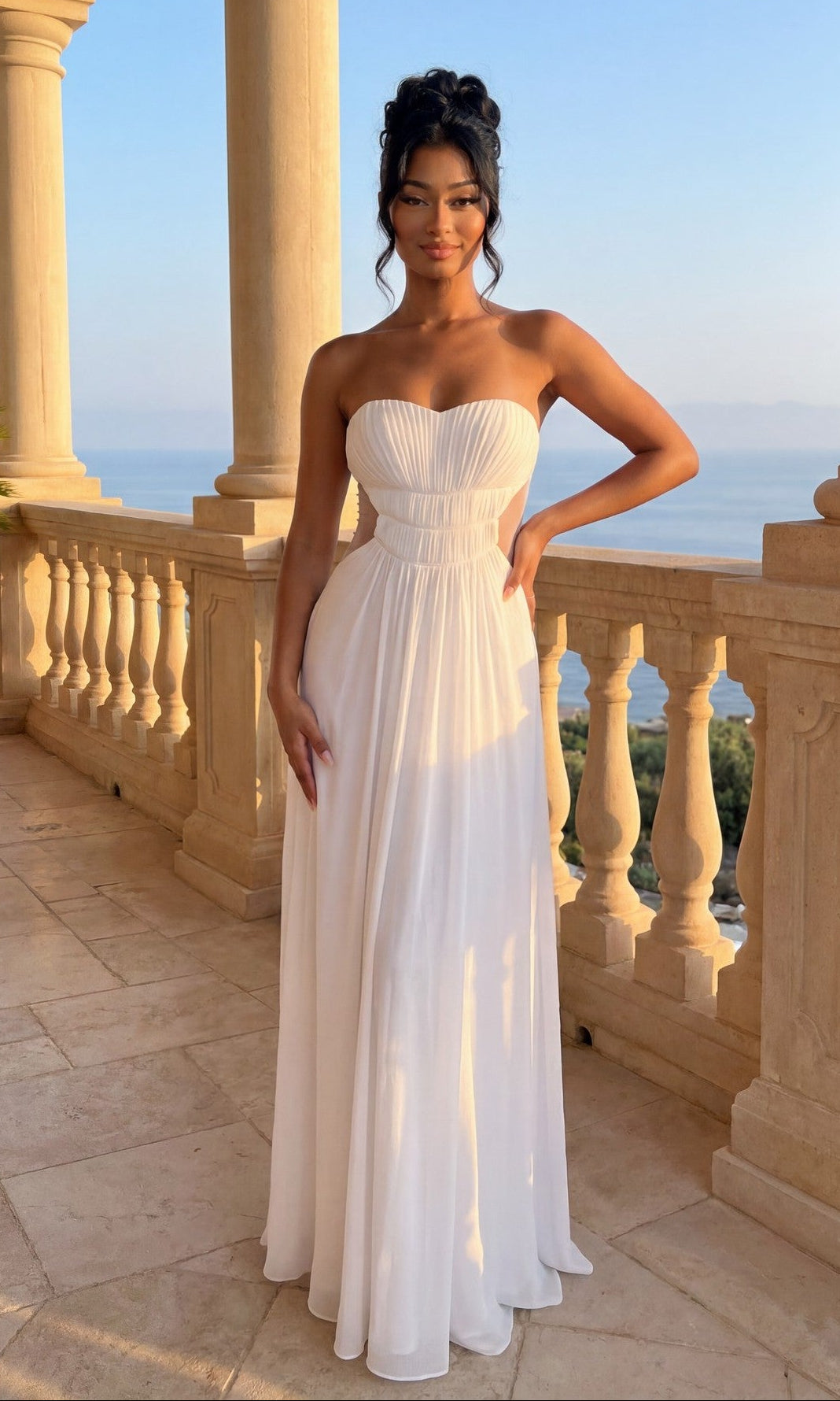 A woman stands on a stone balcony in the La Femme Dress 21184, a strapless sweetheart gown in white, her hair styled up. The scene includes columns, a balustrade, and a scenic outdoor view.