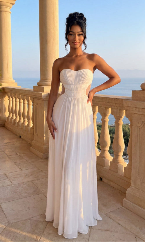 A woman stands on a stone balcony in the La Femme Dress 21184, a strapless sweetheart gown in white, her hair styled up. The scene includes columns, a balustrade, and a scenic outdoor view.