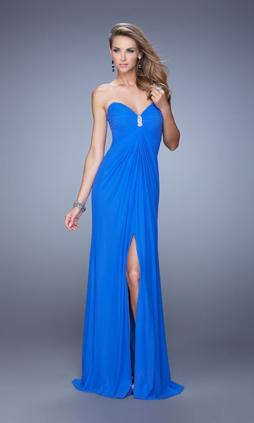 A woman wears the La Femme Dress 21233, a strapless royal blue jersey net gown with a sweetheart neckline, front slit, and embellishments, standing against a plain gray background.