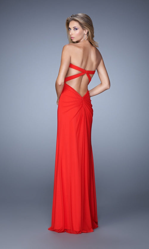 Woman wearing the La Femme Dress 21233, a floor-length red jersey net gown with crisscross straps and a strapless bodice, posing against a plain gray background.