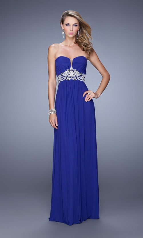 A woman models the Strapless La Femme Ruched Designer Prom Dress 21357, featuring a jeweled waistband, against a plain gray background.