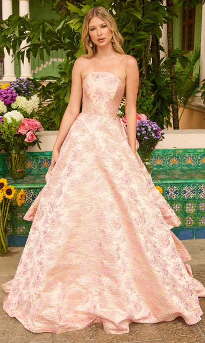 A woman stands outdoors before green foliage and flowers, wearing the Ava Presley 26412 Ruffled Strapless Prom Gown in blush, an A-line evening dress with subtle floral design.