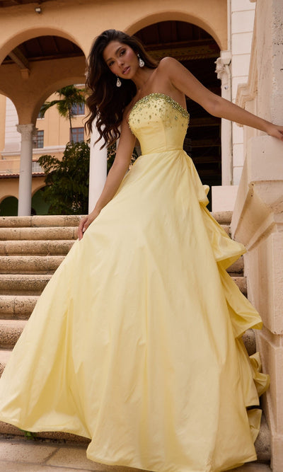 Woman in a Long Prom Dress (Ava Presley 26417) in soft yellow stands on stone steps, wearing a strapless ruffle ball gown with jeweled bodice, in front of an arched building.