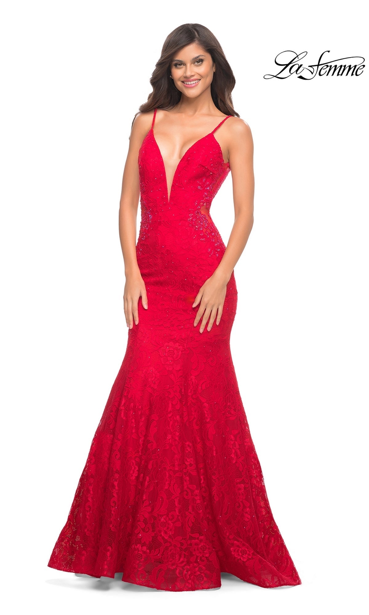 A woman stands smiling in the La Femme Backless Long Lace Prom Dress 28355, featuring a sleeveless, floor-length red lace design with a deep V-neckline, mermaid skirt, and elegant lace detailing.
