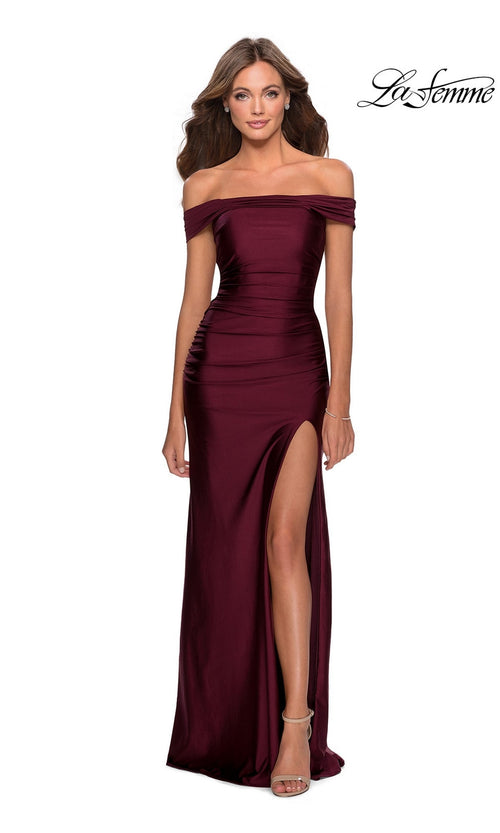 A woman wears the La Femme Strappy-Back Tight Long Prom Dress 28506 in burgundy, featuring an off-the-shoulder neckline, thigh-high slit, and strappy heels. The "La Femme" logo appears in the top right corner.