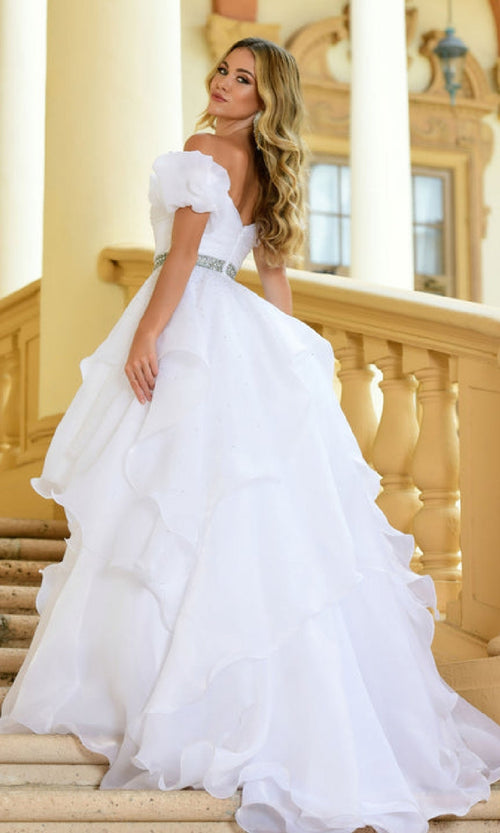 A woman in the Ava Presley 28571 puff-sleeve long prom ball gown stands on a staircase, looking over her shoulder.