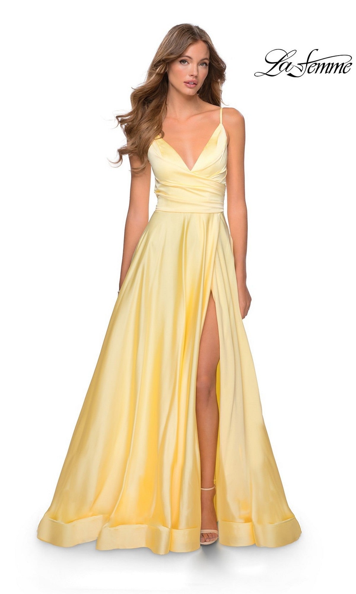 A woman wears the La Femme V-Neck Long A-Line Prom Dress 28607 in pale yellow with a deep V-neckline, thin straps, and a high slit, standing against a white background. The "La Femme" logo is in the top right corner.