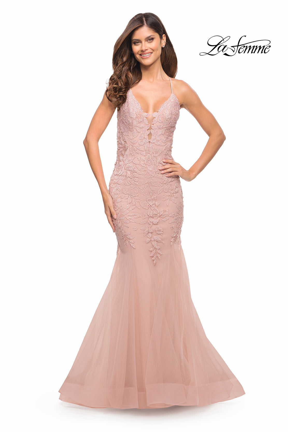 A woman wearing a blush pink Backless Long Lace Mermaid Prom Dress by La Femme with thin straps stands smiling against a white background.