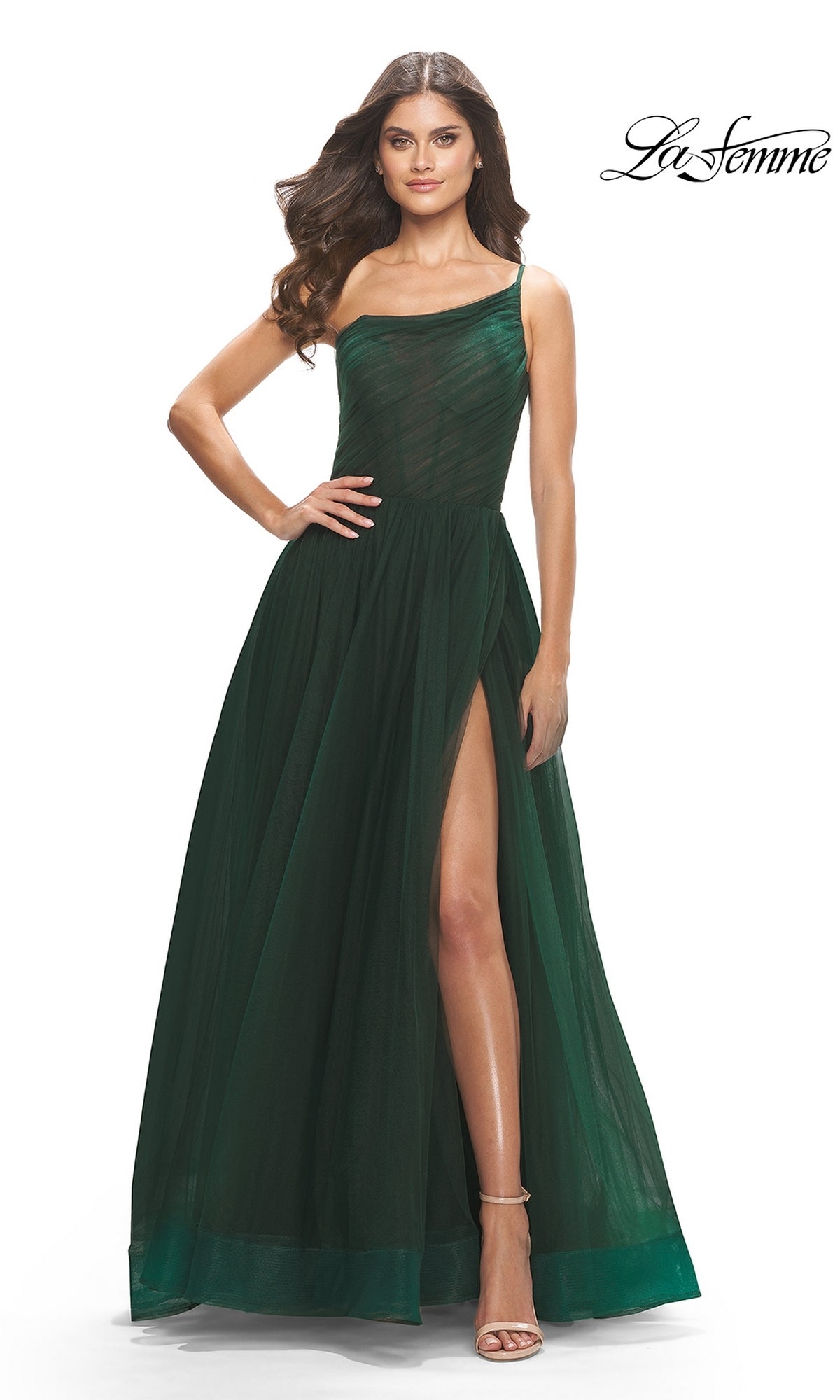 A woman poses gracefully in the One-Shoulder Sheer-Bodice Prom Ball Gown 31069, featuring a dark green hue and high slit, highlighting its elegant design against a white background.
