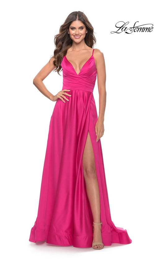 A woman smiles in the La Femme Bright Long A-Line Prom Dress 31121, a floor-length pink gown with a deep V-neckline, side slit, and spaghetti straps. The flowing skirt adds elegance to this designer evening look.