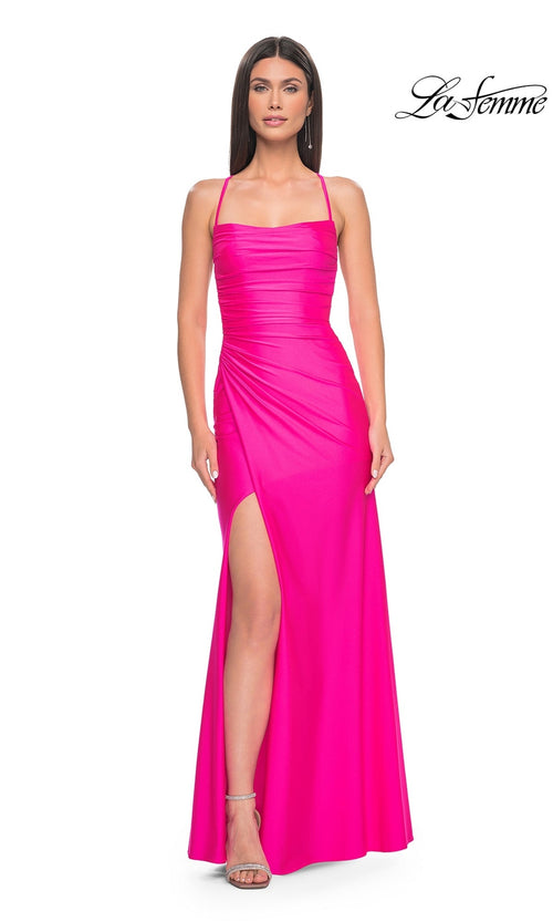 A woman stands against a white background in the La Femme Strappy Open-Back Long Prom Dress 31129 in Neon Pink, featuring spaghetti straps and a thigh-high slit. The La Femme logo appears in the top right corner, highlighting this eye-catching gown.
