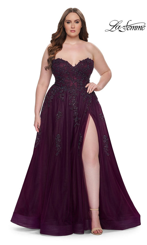 A woman in the La Femme Long Prom Dress 31570, a plus-size strapless gown with a corset bodice, floral embellishments, and a high leg slit, stands against a white background.