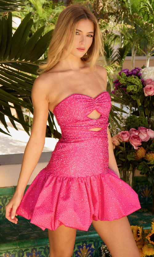 A woman stands outdoors among plants and flowers, wearing the Ava Presley 47222 Cut-Out Short Bubble Hoco Dress—a strapless mini with sparkly pink fabric, cutout details, and a flared bubble skirt.